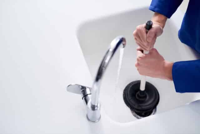 plumber unblocking a drain with a plunger