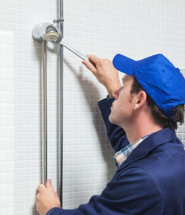 Serious Plumber Repairing Shower Head In Public Bathroom